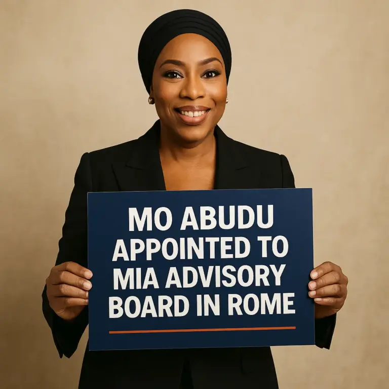 Mo Abudu smiling confidently in a black blazer and headwrap, holding a blue sign announcing her appointment to the MIA Advisory Board in Rome, symbolizing African leadership in global media.